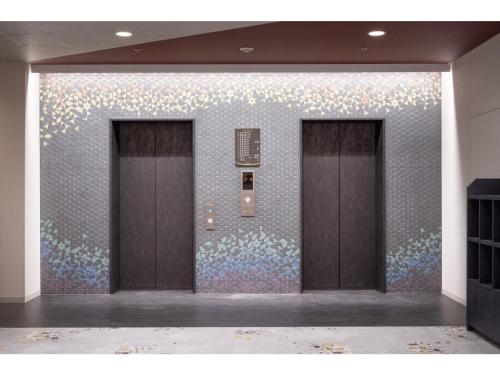 deux ascenseurs dans une pièce avec un mur de fleurs dans l'établissement Smile Hotel Premium Kanazawa Higashiguchi Ekimae - Vacation STAY 73602v, à Housai
