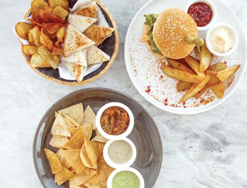 Una mesa con un plato de patatas fritas y una hamburguesa con salsas. en CALIXTA Hotel, en Playa del Carmen