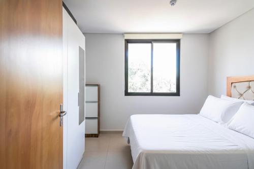 a white bedroom with a bed and a window at Calido 1BR Dpto, a minutos del Aeropuerto in Asuncion