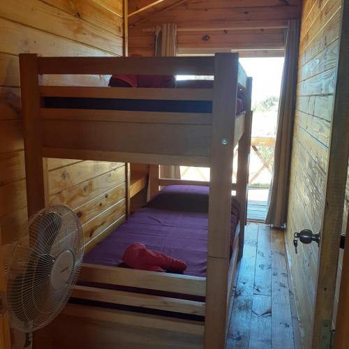 a bunk bed in a wooden room with a fan at Cabañas Batavi in Punta Del Diablo
