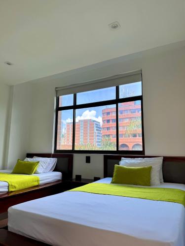 two beds in a room with a large window at Hotel Plaza Mayor 44 in Medellín