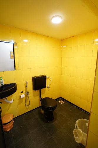 a bathroom with a black toilet and a yellow wall at Paradise A Social Hostel in Anjuna
