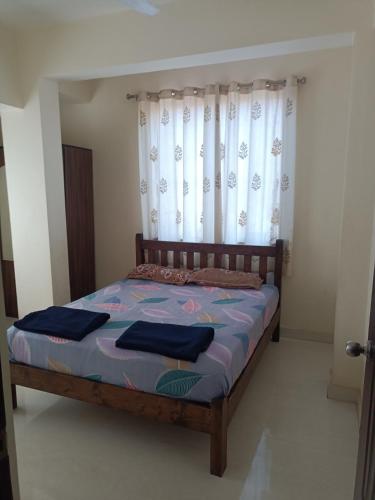 ChicalimGuest House Sai Leela的一间卧室，里面有一张木床，床边挂着窗帘，还有一扇窗户。