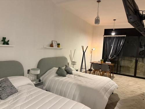 two beds in a white room with a table and a tableablish at Loft ËNXË Boutique Habitación Olivo in Cuetzalán del Progreso