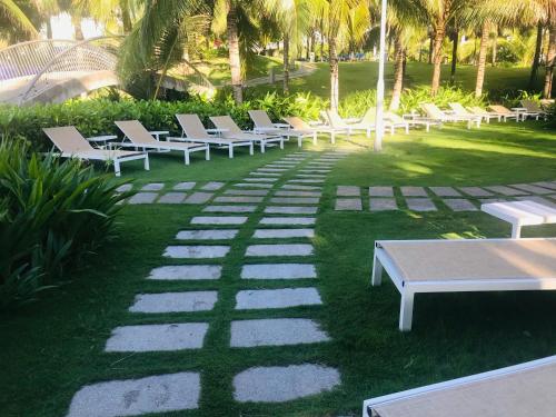 une rangée de bancs blancs sur une pelouse avec des palmiers dans l'établissement Bãi Dài Rerort, à Cam Ranh International Airport