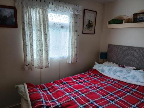 um quarto com uma cama com um cobertor vermelho e uma janela em Charming 6 Berth Caravan With Decking By The Beach In Suffolk Ref 40107Nd em Gunton