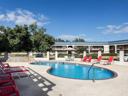 a swimming pool with red chairs and a building at Econo Lodge Grenada in Grenada