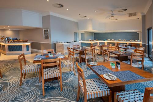 Un restaurante con mesas y sillas de madera y una cocina. en Garden Route Hotel, en Mossel Bay