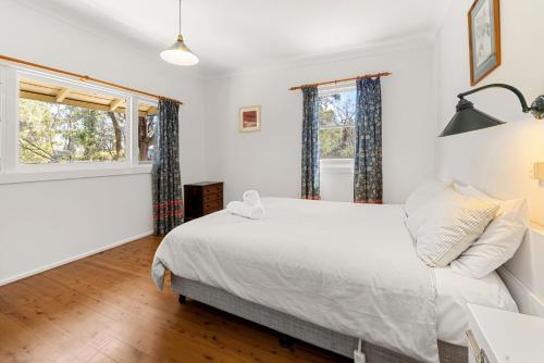 een slaapkamer met een bed en twee ramen bij Banksia Cottage - Pet Friendly Waterfront in Callala Bay