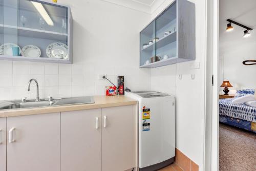 een keuken met witte kasten, een spoelbak en een vaatwasser bij Banksia Cottage - Pet Friendly Waterfront in Callala Bay