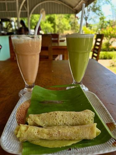 达瓦拉维Maika Safari Lodge的坐在桌子上,一边喝两杯饮料一边吃一盘食物