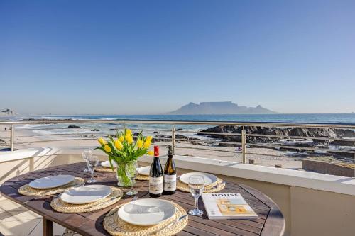 a table with wine bottles and glasses on a balcony overlooking the beach at HOME-LYNN, 4 bedroom, Bloubergstrand in Bloubergstrand