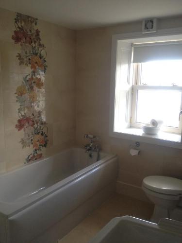 baño con bañera, aseo y ventana en Brownes Town House en Dungarvan
