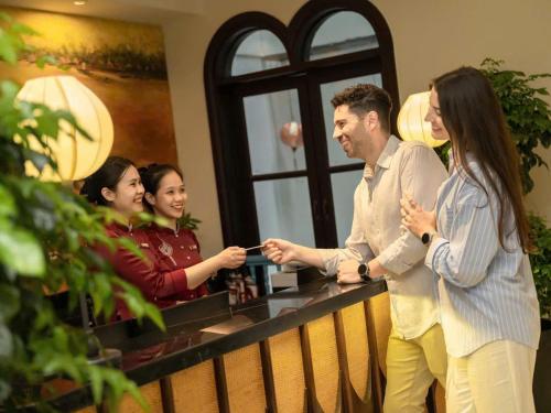 a group of people standing around a counter with a man holding a cell phone at Little Residence - A Boutique Hotel & Spa in Hoi An