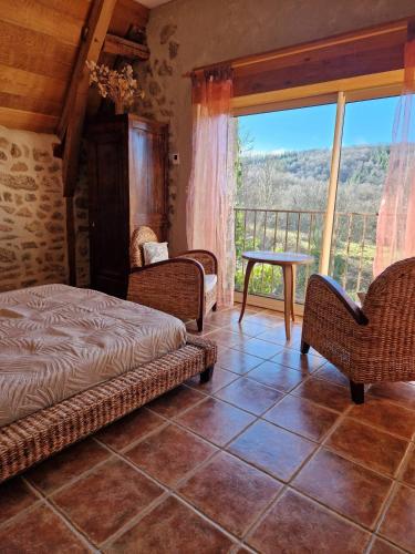 a bedroom with a bed and chairs and a balcony at La Fontaine d'Aubrac in Florentin-la-Capelle