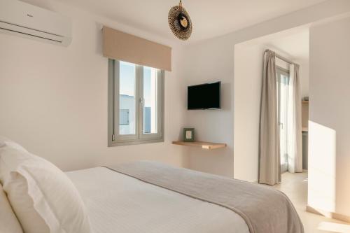 a white bedroom with a bed and a tv at La Maltese Central in Naousa