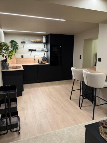 a kitchen with black cabinets and white chairs at Notodden Luxe Apartment in Notodden