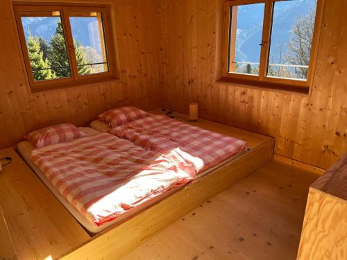 a bed in a wooden room with two windows at Sunnehuesli in Braunwald