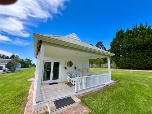 ein weißes Haus mit einer Veranda und einem Rasen in der Unterkunft Cozy Cottage in idyllic greenery in Harkerville