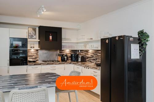 a kitchen with white cabinets and a black refrigerator at Amsterdam Group Villa 20 plus beds 4 - 5 bedrooms in Zwanenburg