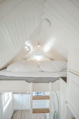 a loft bed in a white room with white pillows at Olenilsøya Mini Villa in Reine