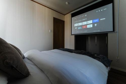 a bedroom with a bed with a flat screen tv on the wall at Dekoboko inn西本町 in Omura