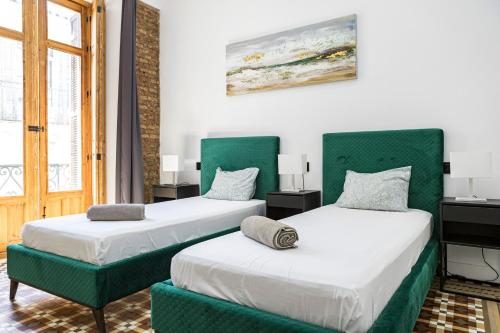 two beds with green accents in a room at NOMADIA en Plaza de la Constitucion 1 in Málaga