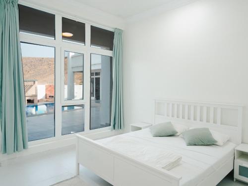 a white bedroom with a bed and a large window at Al-Salam Villa-Family Pool & Private Garden in Misfāh