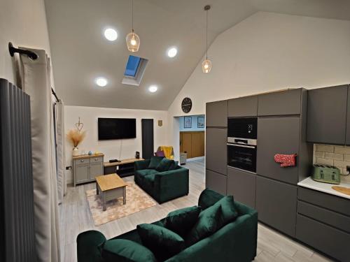 a living room with two green couches and a kitchen at 4 bedroom bungalow in Kettering - Garden - Parking - WiFi in Kettering