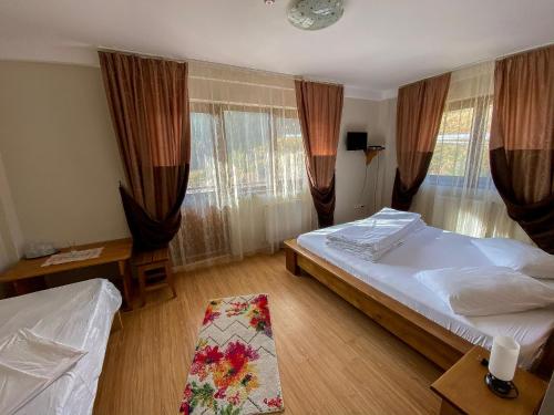 ein Schlafzimmer mit zwei Betten und einem Tisch und Fenstern in der Unterkunft Pensiunea Turistică Octavian in Moroeni