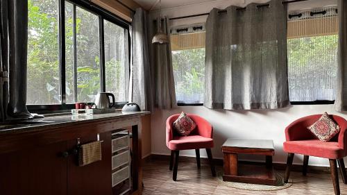 two red chairs sitting in a kitchen with windows at The Burrow in South Goa. in Dabolim