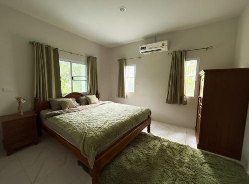 Schlafzimmer mit einem Bett mit grüner Decke und Fenstern in der Unterkunft Cozy Bungalow in Ban Nua
