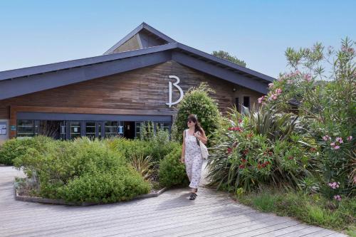 une femme marchant sur une promenade en bois devant un bâtiment dans l'établissement Belambra Clubs Seignosse Les Estagnots, à Seignosse