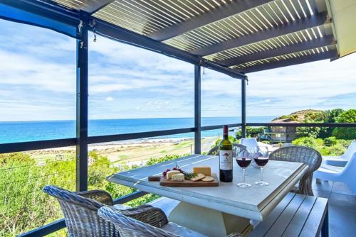 a table with wine glasses and a plate of food on a balcony at Stunning Views & Renovated Beach Chic in Carrickalinga