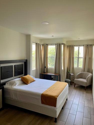 a bedroom with a bed and a chair and windows at Hotel Villa Serena San Benito in San Salvador