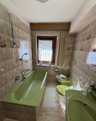 a bathroom with a green tub and two toilets at Ciasa Nives in La Villa