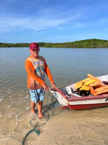 a man is standing in the water next to a boat at Pousada Rosa de Saron - Algodoal in Algodoal