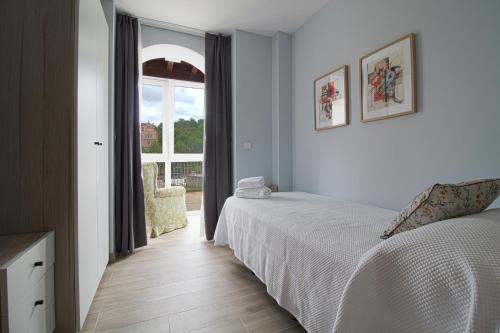 een witte slaapkamer met een bed en een raam bij Apartamentos Turísticos La Pontificia in Comillas