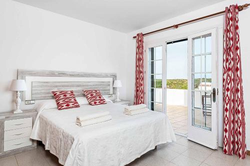 a white bedroom with a bed with red pillows at Villa Cala Llonga in Cala Llonga