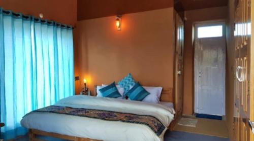 a bedroom with a bed with blue curtains and a window at Buransh Retreat in Jageshwar