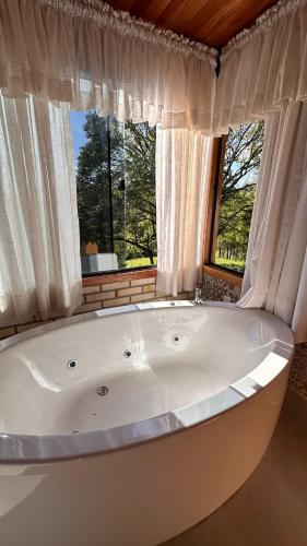 eine große weiße Badewanne in einem Zimmer mit Fenster in der Unterkunft Chale Pedra do Sol in Caxias do Sul