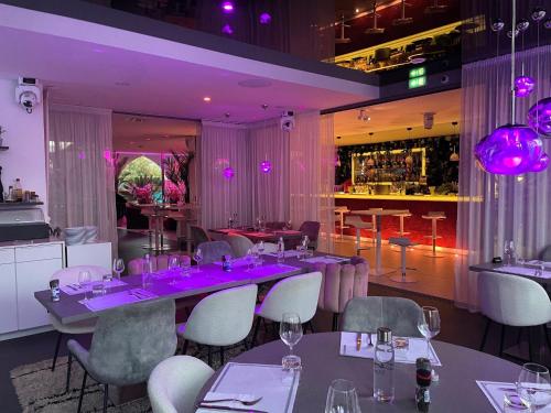 een restaurant met tafels en stoelen en paarse verlichting bij Oz'Inn Hôtel & Spa in Cap d'Agde