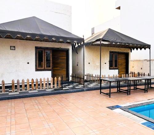 a building with tables and umbrellas next to a pool at The Starlight Farmstay- Poolside Tent Stay in Jaipur in Jāmb