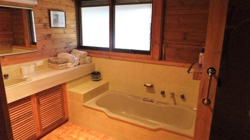 La salle de bains est pourvue d'une baignoire, d'un lavabo et d'une fenêtre. dans l'établissement Gunyah Valley Retreat, à Goornong