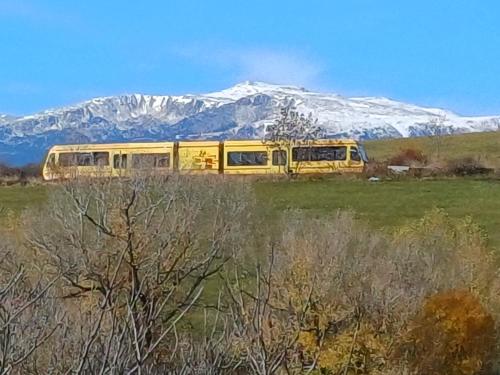 a yellow bus in a field with a snow covered mountain at Le panoramique in Saillagouse
