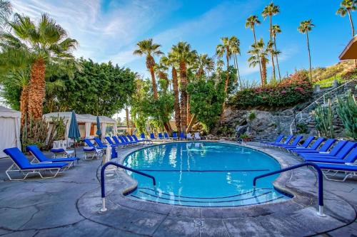 a swimming pool with blue chairs and palm trees at Palm Springs Tennis Club in Palm Springs