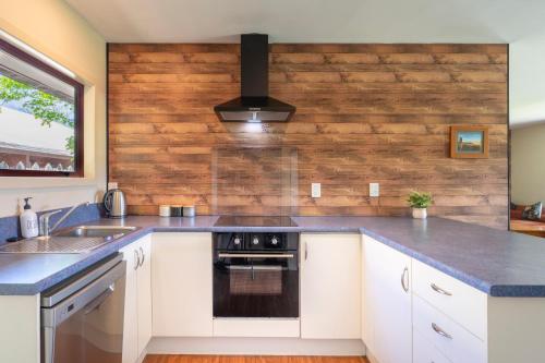 a kitchen with white cabinets and a wooden wall at Cozy, Functional,Private - HS65214 in Hanmer Springs