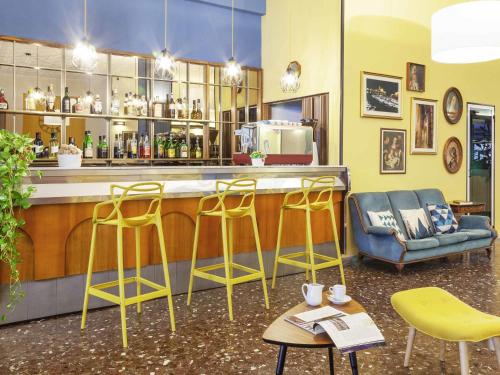 Una barra con tres taburetes amarillos y un mostrador. en ibis styles Trani, en Trani