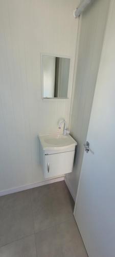 a white bathroom with a sink and a mirror at Refúgio ensolarado a poucos passos do mar in Navegantes