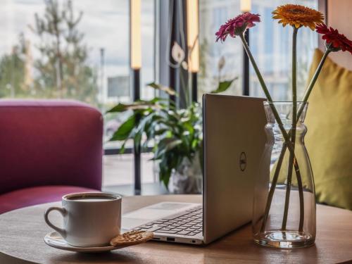 ein Tisch mit einem Laptop und einer Tasse Kaffee und Blumen in der Unterkunft Ibis Aktobe in Aqtöbe